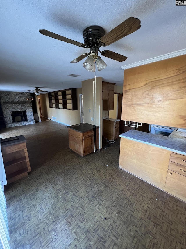 kitchen featuring a textured ceiling, a stone fireplace, ceiling fan, and dark parquet floors