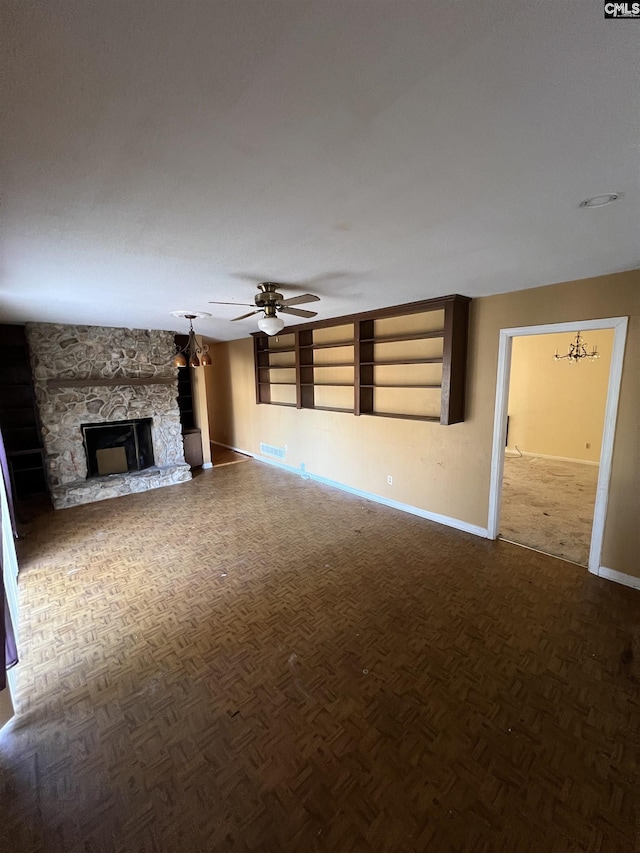 unfurnished living room featuring built in shelves, parquet floors, a fireplace, and ceiling fan with notable chandelier