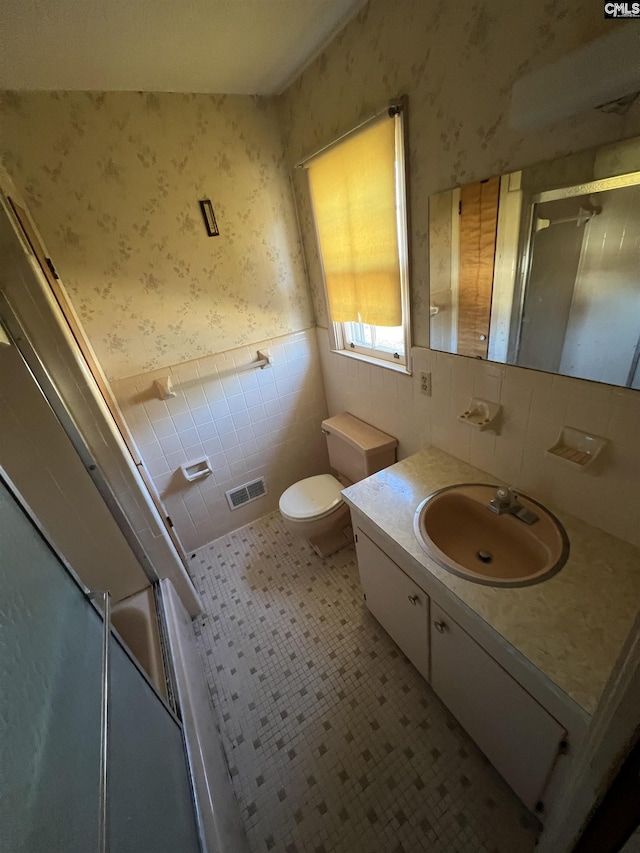 bathroom featuring toilet, vanity, tile patterned floors, and tile walls