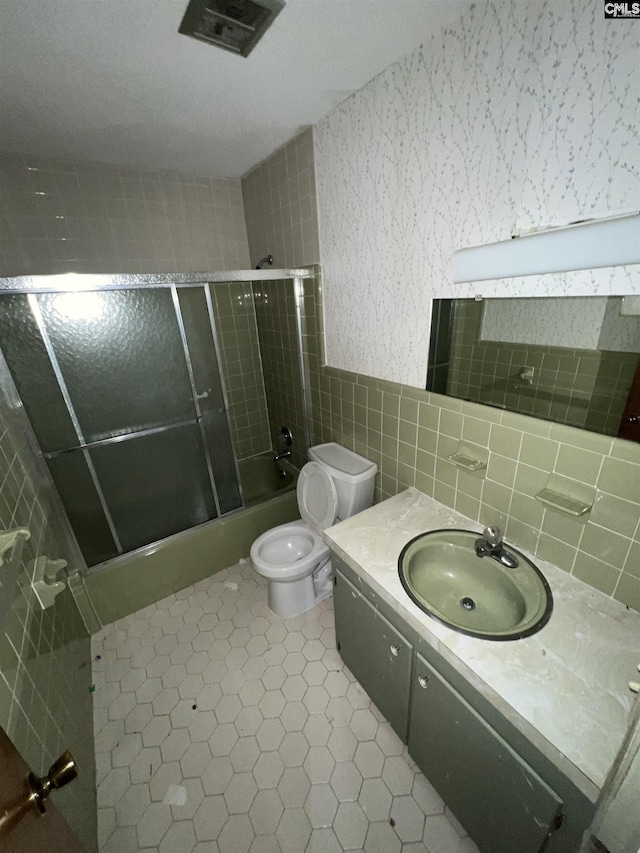 full bathroom featuring tile patterned flooring, combined bath / shower with glass door, toilet, vanity, and tile walls