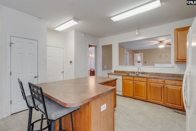 kitchen with ceiling fan, dishwasher, sink, a breakfast bar area, and a kitchen island