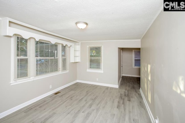 empty room with built in features, light hardwood / wood-style floors, and a textured ceiling