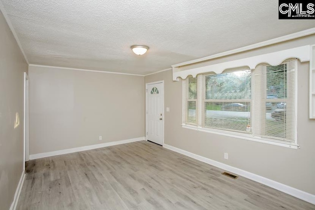 spare room featuring light hardwood / wood-style flooring, a textured ceiling, and ornamental molding