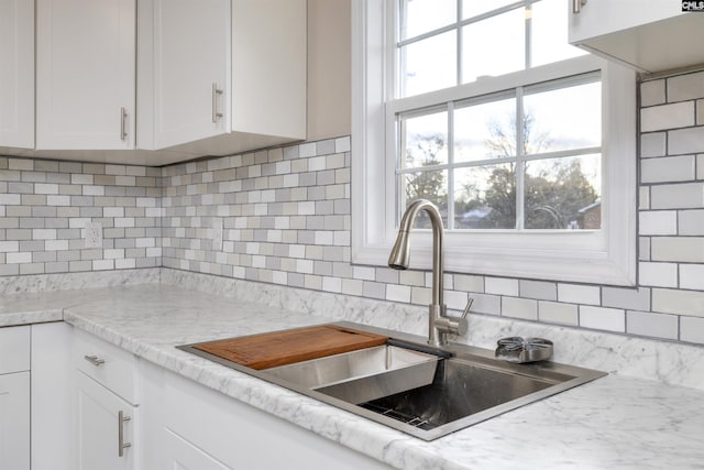 kitchen with white cabinets, light countertops, a sink, and decorative backsplash