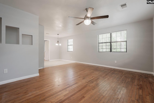 empty room with wood-type flooring and ceiling fan with notable chandelier