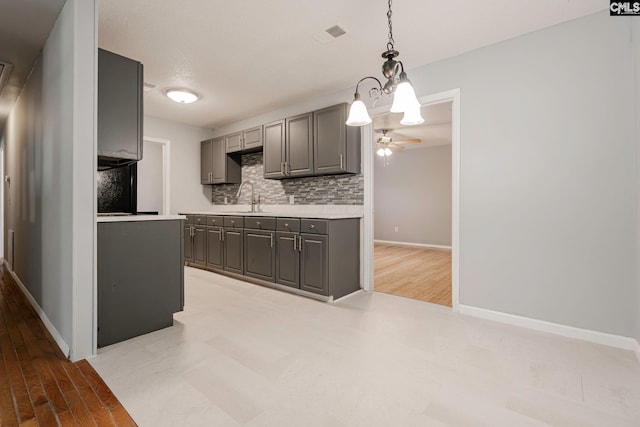 kitchen featuring gray cabinetry, sink, tasteful backsplash, decorative light fixtures, and ceiling fan with notable chandelier