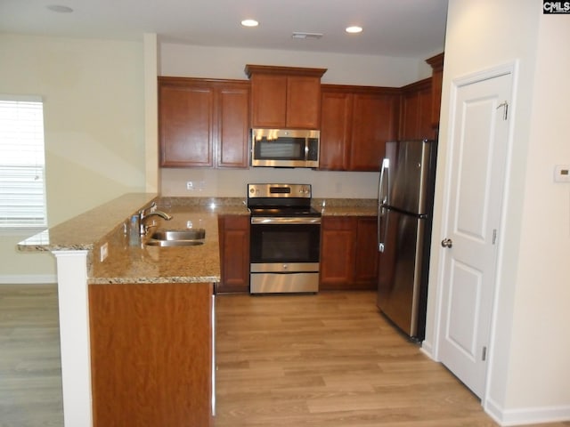 kitchen featuring sink, stainless steel appliances, light stone counters, kitchen peninsula, and light wood-type flooring