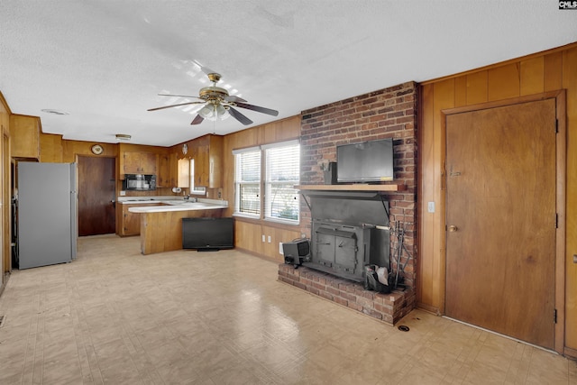 kitchen with a wood stove, ceiling fan, a center island, white fridge, and wooden walls