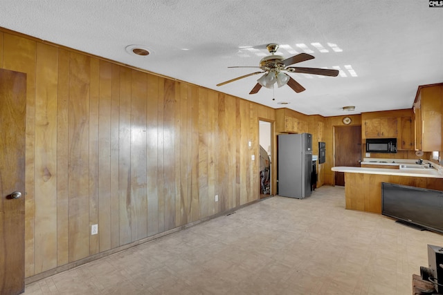 kitchen with wood walls, ceiling fan, stainless steel fridge, and kitchen peninsula