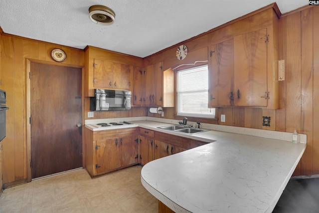 kitchen with kitchen peninsula, wooden walls, sink, and black appliances