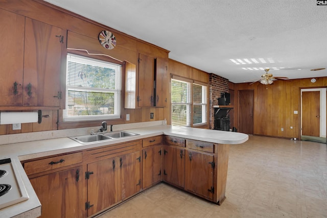 kitchen with kitchen peninsula, a textured ceiling, ceiling fan, wooden walls, and sink