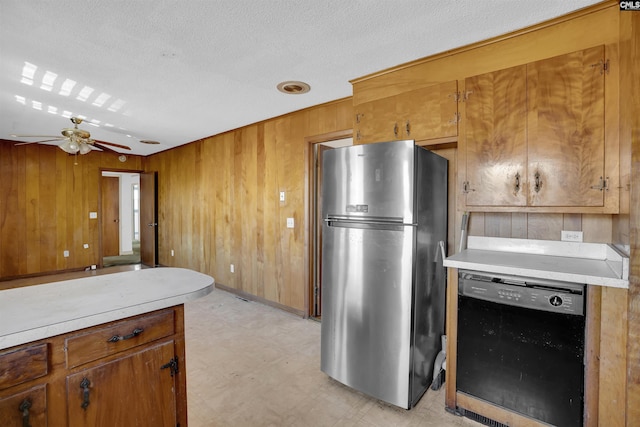 kitchen with wooden walls, ceiling fan, black dishwasher, a textured ceiling, and stainless steel refrigerator