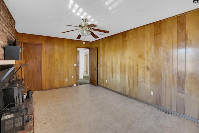 unfurnished living room featuring wooden walls, ceiling fan, and a textured ceiling