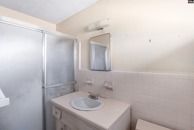 bathroom with a textured ceiling, toilet, a shower with door, vanity, and tile walls