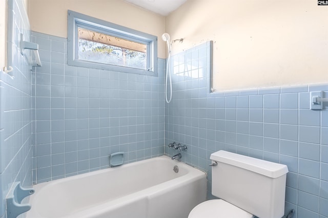 bathroom featuring tiled shower / bath combo, toilet, and tile walls