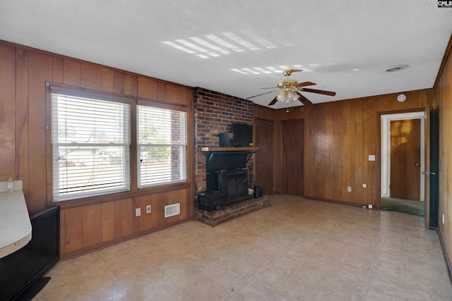 unfurnished living room with a wood stove, ceiling fan, wooden walls, and a textured ceiling