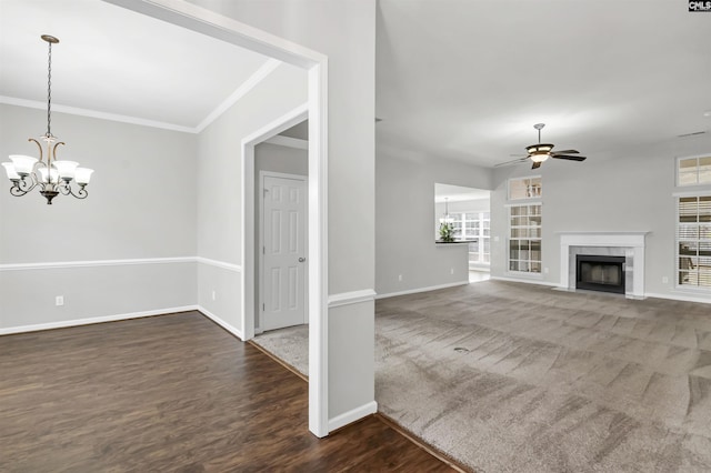 unfurnished living room featuring ceiling fan with notable chandelier, dark wood-type flooring, ornamental molding, and a tiled fireplace