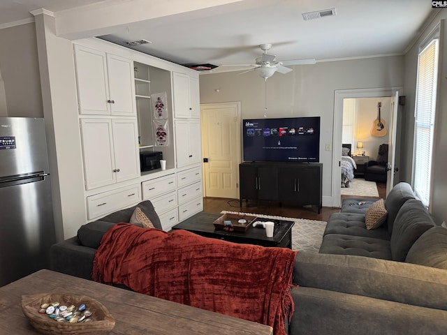 living room featuring ceiling fan, a healthy amount of sunlight, ornamental molding, and dark wood-type flooring