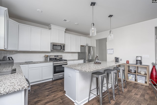 kitchen featuring hanging light fixtures, decorative backsplash, appliances with stainless steel finishes, a kitchen island, and white cabinetry