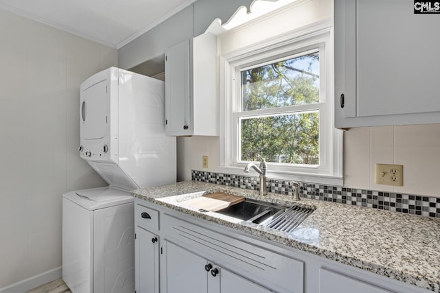 laundry room with stacked washing maching and dryer, crown molding, and sink