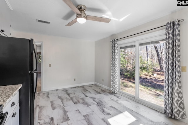 kitchen with white cabinets, ceiling fan, black refrigerator, and light stone countertops