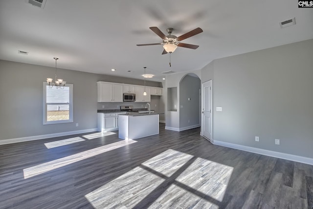 unfurnished living room with visible vents, a sink, dark wood finished floors, arched walkways, and baseboards