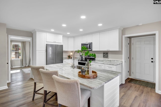 kitchen featuring light stone counters, stainless steel appliances, light hardwood / wood-style floors, white cabinetry, and a breakfast bar area