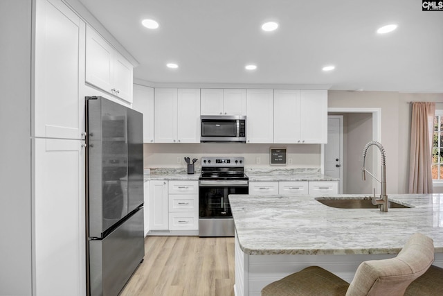 kitchen with light stone countertops, appliances with stainless steel finishes, white cabinets, and sink