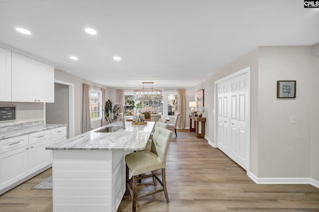 kitchen featuring sink, light stone counters, a breakfast bar area, a kitchen island with sink, and white cabinets