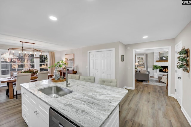 kitchen featuring dishwasher, a center island with sink, sink, light stone countertops, and white cabinetry