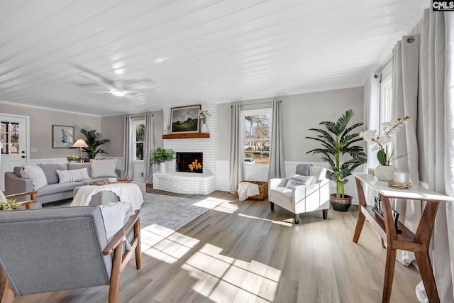 living room featuring ceiling fan, wooden ceiling, light hardwood / wood-style flooring, crown molding, and a fireplace