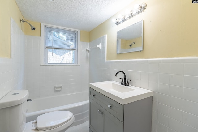 full bathroom with vanity, tiled shower / bath combo, toilet, a textured ceiling, and tile walls