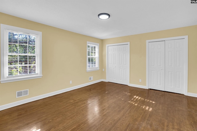 unfurnished bedroom with dark wood-type flooring, multiple windows, and multiple closets