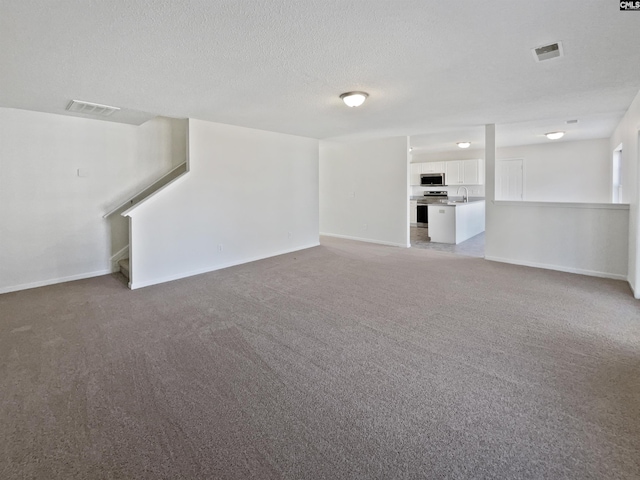 unfurnished living room with a textured ceiling, carpet floors, and sink