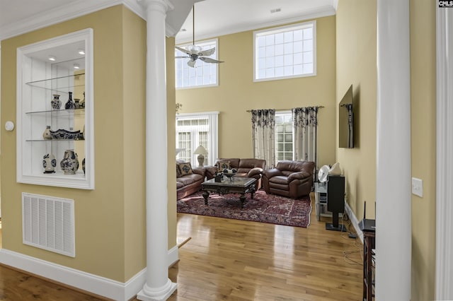 living room with ceiling fan, wood-type flooring, ornate columns, and crown molding