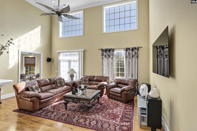 living room with ceiling fan, a towering ceiling, crown molding, and light hardwood / wood-style flooring