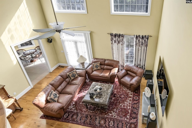 living room featuring ceiling fan, a towering ceiling, and light wood-type flooring