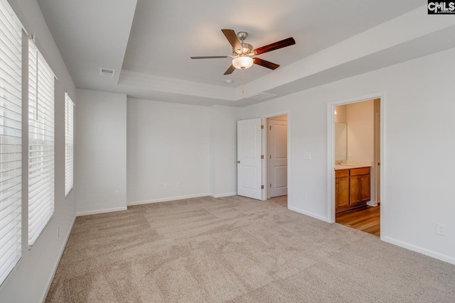 empty room with ceiling fan, a raised ceiling, and light carpet