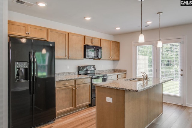 kitchen with black appliances, sink, an island with sink, decorative light fixtures, and light stone counters