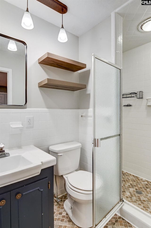 bathroom with vanity, a shower with door, tile patterned floors, toilet, and tile walls