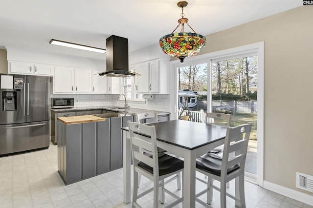 kitchen with backsplash, white cabinets, sink, island exhaust hood, and stainless steel appliances