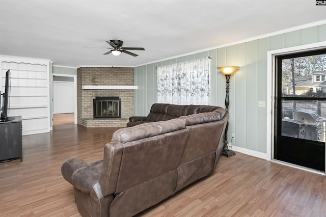 living room featuring ceiling fan, wood-type flooring, ornamental molding, and a brick fireplace