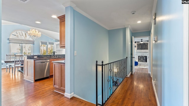 corridor with crown molding, sink, an inviting chandelier, light hardwood / wood-style floors, and lofted ceiling