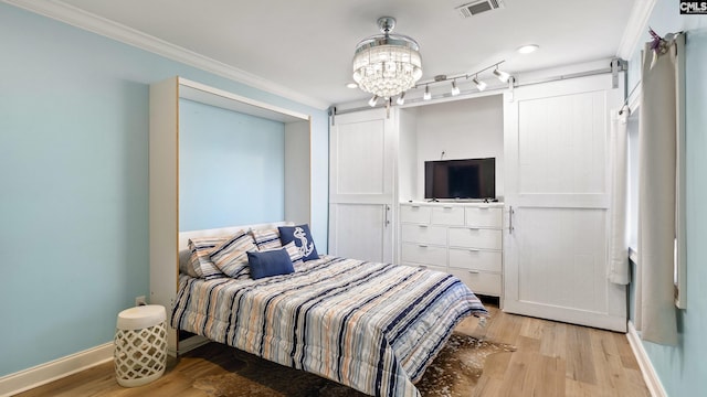 bedroom with a barn door, a chandelier, light hardwood / wood-style floors, and ornamental molding