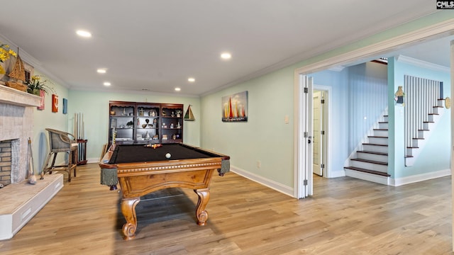 recreation room with a tiled fireplace, light hardwood / wood-style floors, ornamental molding, and billiards