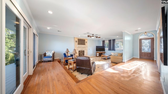 living room with a large fireplace, light hardwood / wood-style floors, ceiling fan, and crown molding