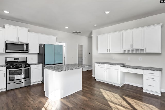 kitchen with stainless steel appliances, dark wood-type flooring, dark stone countertops, white cabinets, and a kitchen island