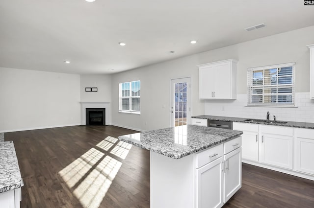 kitchen with a kitchen island, light stone counters, white cabinetry, and sink