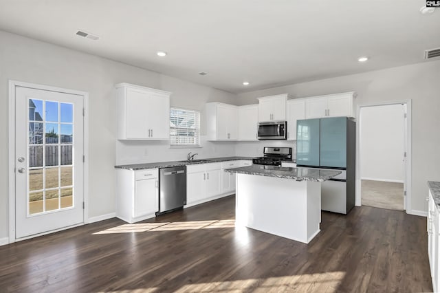 kitchen with dark wood-type flooring, stainless steel appliances, a kitchen island, dark stone counters, and white cabinets