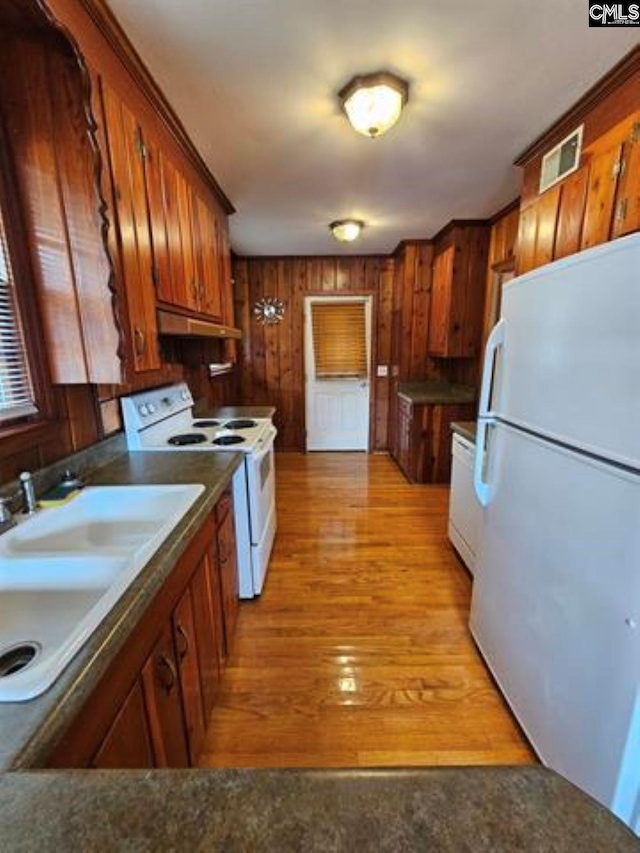 kitchen with light wood-type flooring, white appliances, sink, and wooden walls